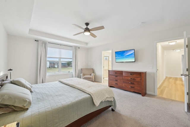 bedroom with ensuite bathroom, carpet floors, a ceiling fan, baseboards, and a raised ceiling