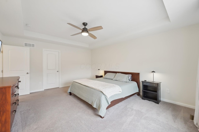 bedroom with carpet floors, a tray ceiling, visible vents, and baseboards