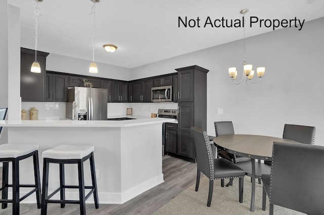 kitchen with backsplash, appliances with stainless steel finishes, light wood-style floors, a peninsula, and a kitchen breakfast bar