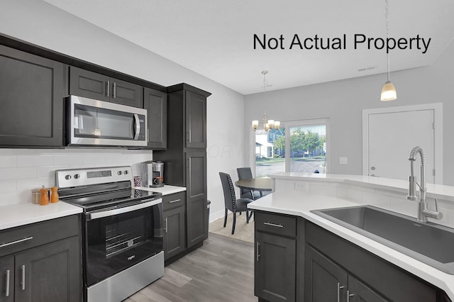 kitchen featuring decorative light fixtures, stainless steel appliances, decorative backsplash, a sink, and a chandelier