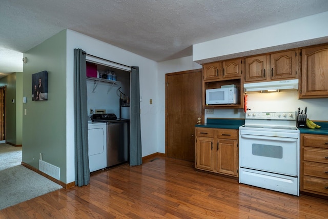 kitchen featuring white appliances, visible vents, washer and clothes dryer, dark wood-style floors, and under cabinet range hood