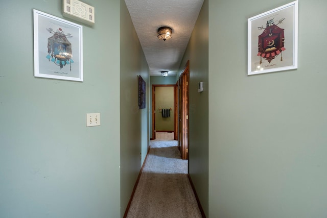 corridor featuring a textured ceiling, carpet floors, and baseboards