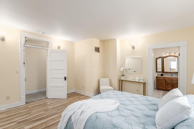 bedroom with a sink, visible vents, baseboards, light wood-style floors, and ensuite bath