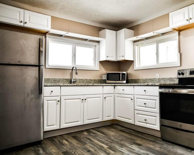 kitchen with dark stone counters, appliances with stainless steel finishes, dark wood-style floors, white cabinetry, and a sink