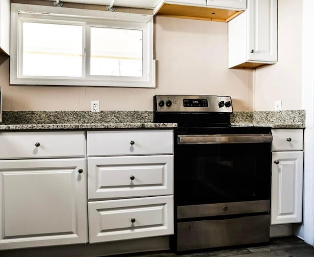 kitchen with dark wood finished floors, stainless steel electric stove, white cabinetry, and dark stone counters