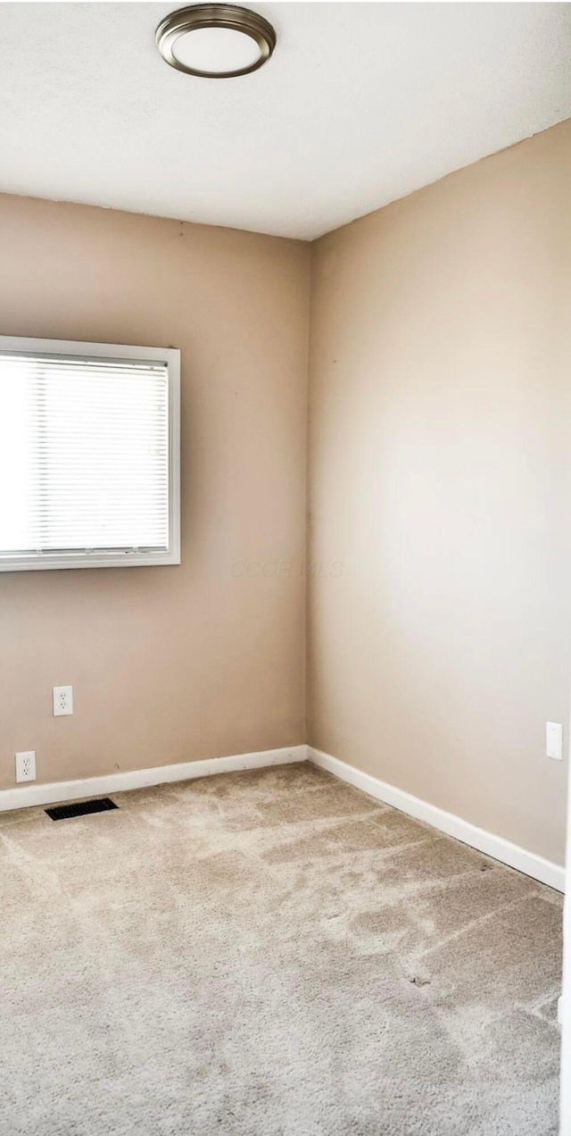 empty room with carpet flooring, visible vents, and baseboards