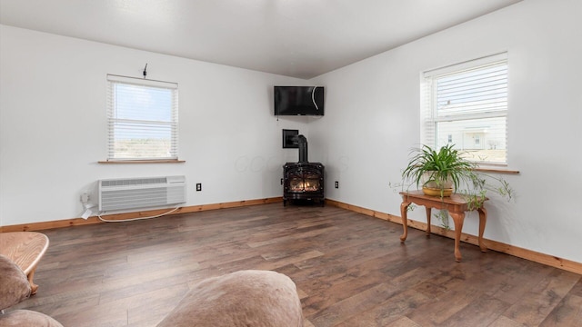 sitting room featuring a wall unit AC, a wood stove, a healthy amount of sunlight, and wood finished floors
