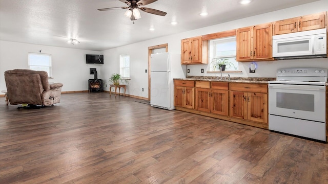 kitchen with a wood stove, white appliances, dark wood finished floors, and a wealth of natural light
