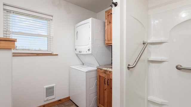laundry area featuring stacked washer and dryer, visible vents, cabinet space, tile patterned flooring, and baseboards