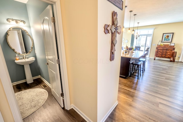 corridor with an inviting chandelier, wood finished floors, baseboards, and visible vents