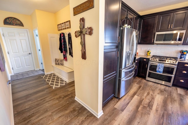 kitchen featuring wood finished floors, baseboards, stainless steel appliances, dark brown cabinets, and backsplash