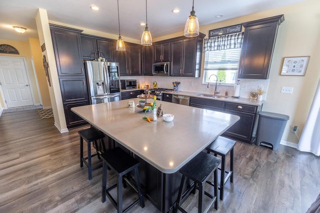 kitchen with a breakfast bar area, dark wood-style floors, a sink, appliances with stainless steel finishes, and tasteful backsplash