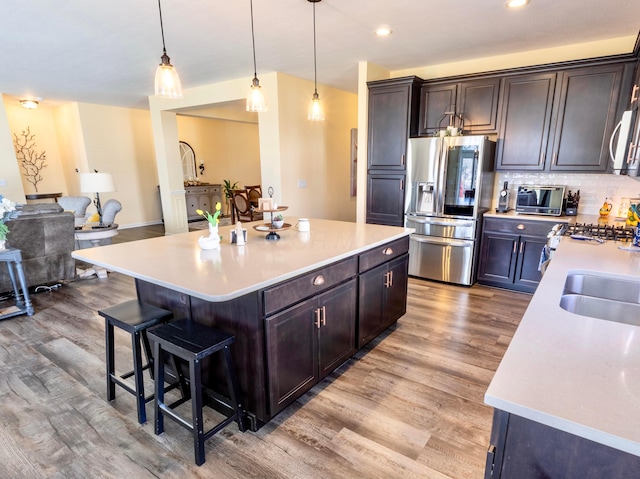 kitchen with stainless steel fridge with ice dispenser, light countertops, decorative backsplash, a kitchen breakfast bar, and light wood-style floors