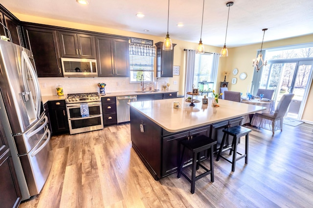 kitchen with a kitchen breakfast bar, light wood finished floors, appliances with stainless steel finishes, and a sink