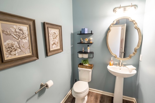 half bath with toilet, baseboards, and wood finished floors