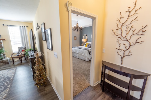 hallway featuring dark wood-style floors, a chandelier, and baseboards