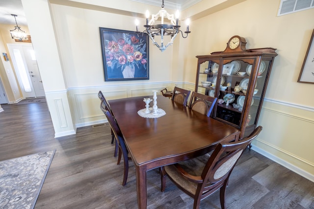 dining space featuring wood finished floors, visible vents, an inviting chandelier, crown molding, and a decorative wall