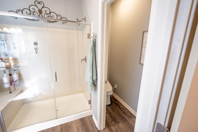 bathroom with a stall shower, toilet, baseboards, and wood finished floors