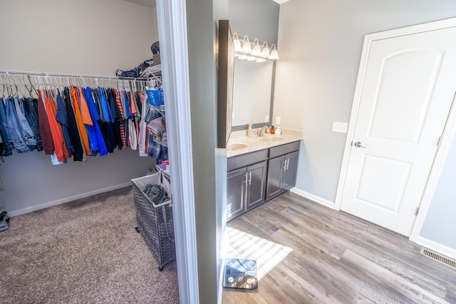 bathroom with visible vents, a walk in closet, wood finished floors, baseboards, and vanity