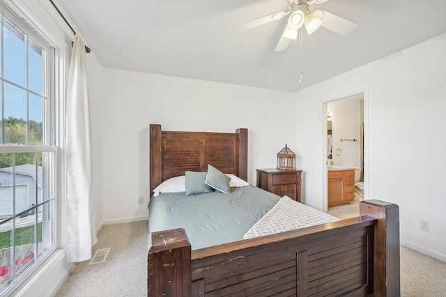 bedroom with ceiling fan, light colored carpet, visible vents, baseboards, and ensuite bath