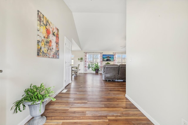 hallway featuring vaulted ceiling, wood finished floors, and baseboards