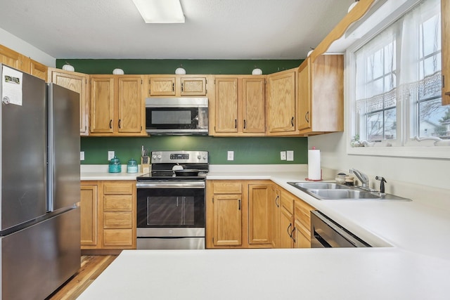 kitchen with stainless steel appliances, wood finished floors, a sink, and light countertops