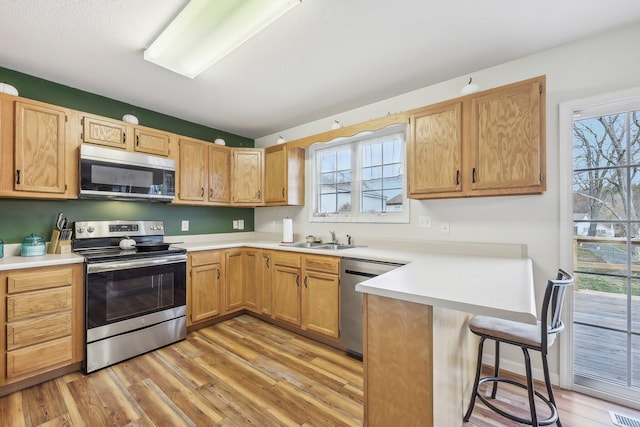 kitchen with a breakfast bar area, appliances with stainless steel finishes, light wood-style floors, a sink, and a peninsula