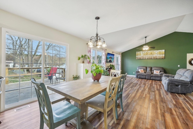 dining space with ceiling fan with notable chandelier, wood finished floors, visible vents, baseboards, and vaulted ceiling