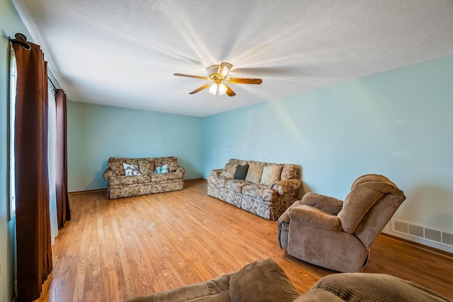 living room with visible vents, a ceiling fan, a textured ceiling, wood finished floors, and baseboards