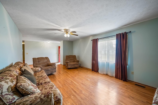 living area featuring light wood-style flooring, visible vents, ceiling fan, and a textured ceiling