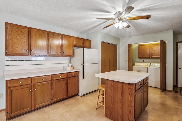 kitchen featuring brown cabinetry, freestanding refrigerator, light countertops, light floors, and washing machine and dryer