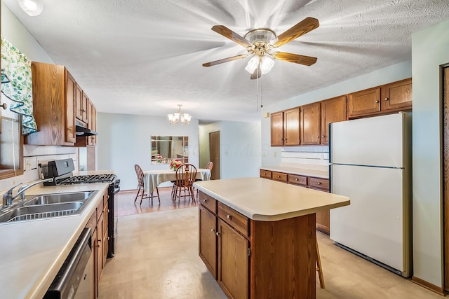 kitchen featuring brown cabinets, freestanding refrigerator, light countertops, under cabinet range hood, and a sink