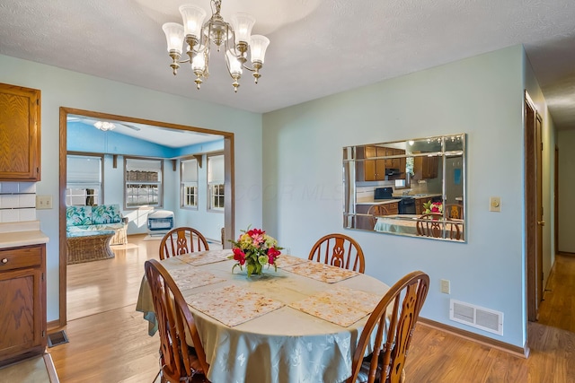 dining area featuring a notable chandelier, light wood finished floors, visible vents, a textured ceiling, and baseboards