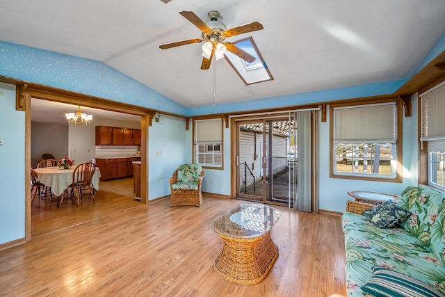 living room featuring lofted ceiling with skylight, baseboards, light wood-style floors, and ceiling fan with notable chandelier