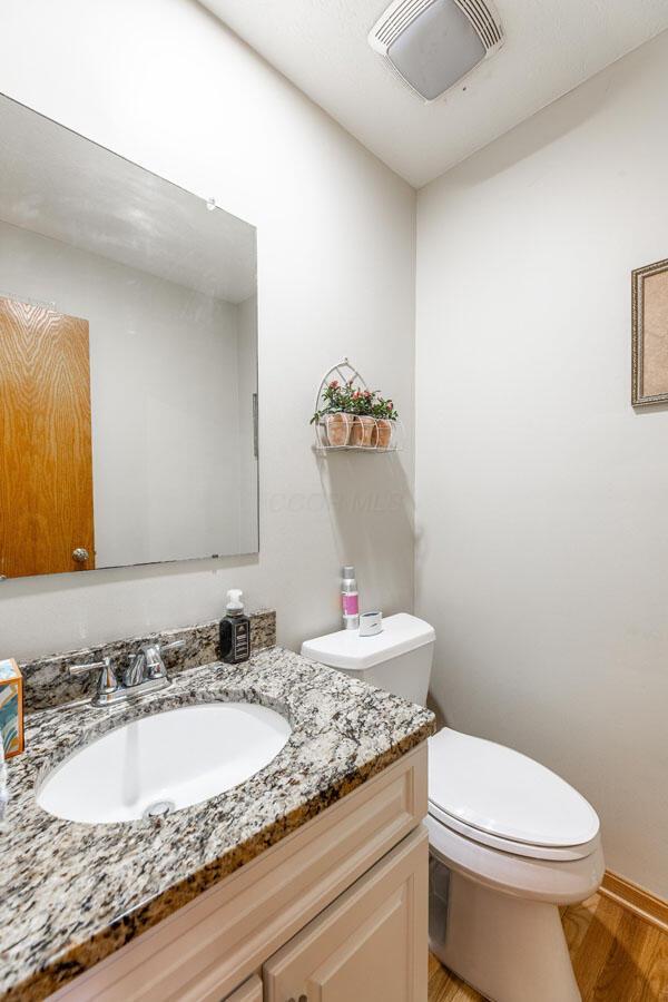 half bathroom with visible vents, wood finished floors, toilet, and vanity