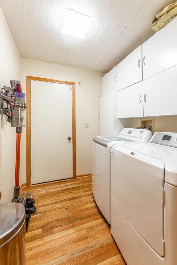 laundry area with cabinet space, a textured ceiling, independent washer and dryer, and light wood-style floors