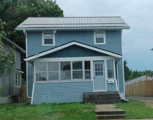 view of front of home with metal roof, a sunroom, entry steps, and fence