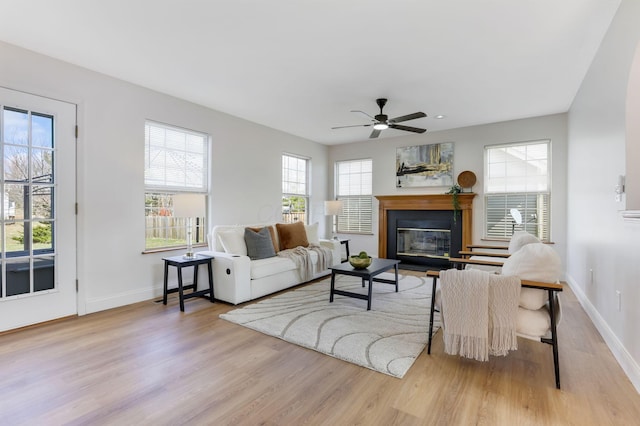 living area with a glass covered fireplace, baseboards, wood finished floors, and a ceiling fan