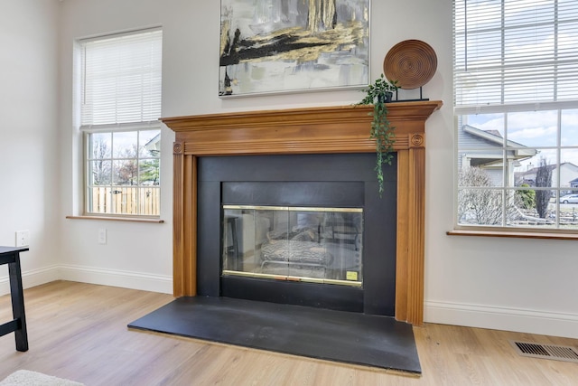 interior details featuring a glass covered fireplace, visible vents, baseboards, and wood finished floors