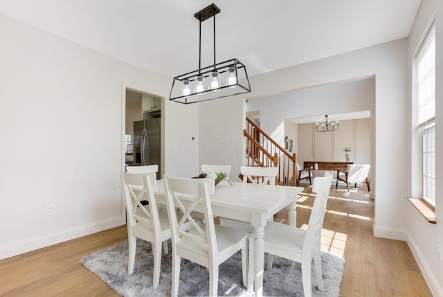 dining room with stairs, an inviting chandelier, plenty of natural light, and light wood-style floors