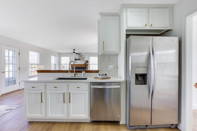 kitchen featuring light countertops, light wood-style flooring, a peninsula, stainless steel appliances, and a sink