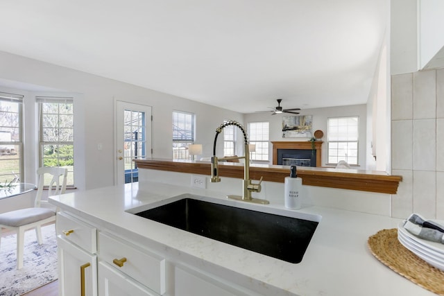 kitchen with ceiling fan, light stone counters, a fireplace, white cabinetry, and a sink