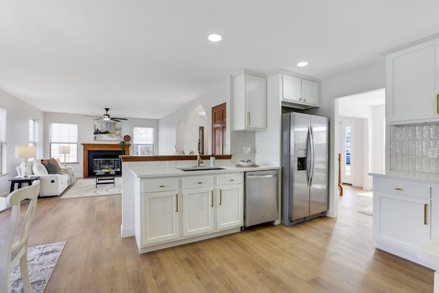 kitchen featuring light wood-type flooring, decorative backsplash, appliances with stainless steel finishes, a glass covered fireplace, and white cabinets