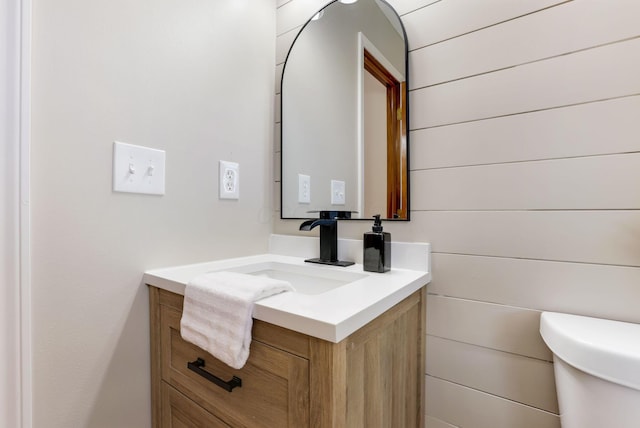 bathroom with wooden walls, toilet, and vanity