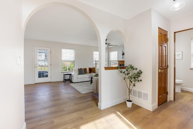 corridor with light wood-type flooring, visible vents, arched walkways, and baseboards