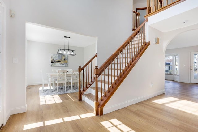 stairway featuring wood finished floors, arched walkways, a towering ceiling, and baseboards