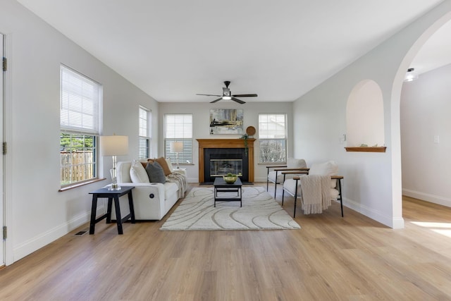 living room with ceiling fan, baseboards, a fireplace with flush hearth, wood finished floors, and arched walkways