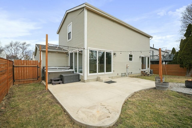 back of house featuring entry steps, a hot tub, a fenced backyard, a yard, and a patio area