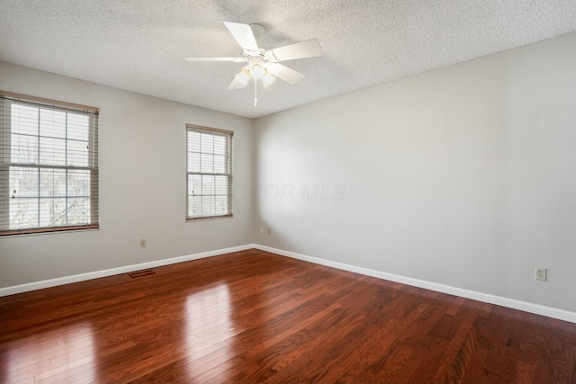 empty room featuring visible vents, a ceiling fan, a textured ceiling, wood finished floors, and baseboards