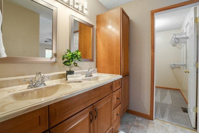 bathroom with a sink, baseboards, a textured ceiling, and double vanity